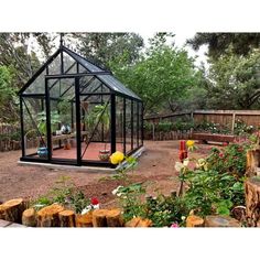 a small black greenhouse in the middle of a garden with lots of flowers and trees