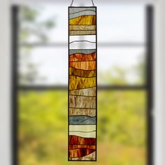 a stained glass wind chime hanging in front of a window with grass and trees outside