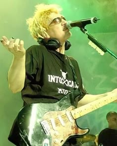 a man with headphones on singing into a microphone and holding a guitar in front of him