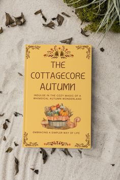 a book sitting on top of a sandy beach next to leaves and grass, with the title'the cottagecorre autumn'written above it