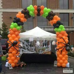 an orange and black balloon arch in the middle of a parking lot with people standing under it