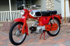 a red motorcycle parked on top of a brick road next to a building with white trim