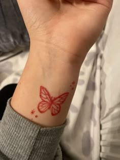 a woman's wrist with a red butterfly tattoo on the left side of her arm