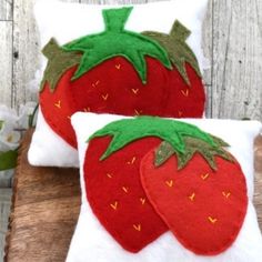 two pillows made to look like strawberries are sitting on a wooden table next to each other