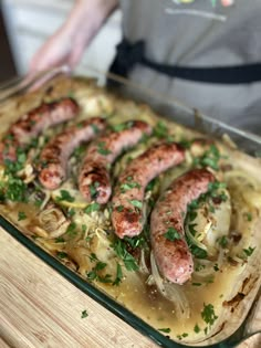 sausages and onions are being cooked in a casserole dish on a cutting board