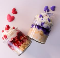 two jars filled with desserts sitting on top of a white table next to hearts