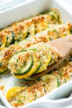 zucchini and cheese casserole in a white dish with a wooden spoon