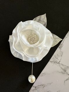 a white flower on a black table next to a marble slab with a pearl brooch in the center