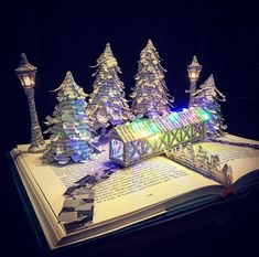 an open book with lights on it and trees in the pages, all lit up