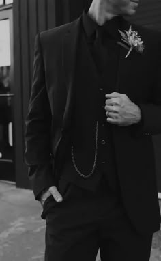 a man in a suit and tie standing next to a building with a flower on his lapel