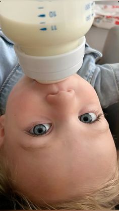 a baby with blue eyes is being held up to its head by an infant bottle