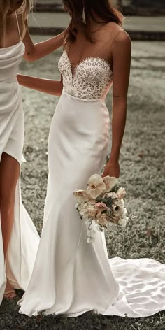 two women in white dresses standing next to each other and one is holding a bouquet