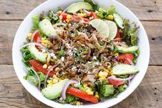 a white bowl filled with salad topped with meat and veggies on top of a wooden table