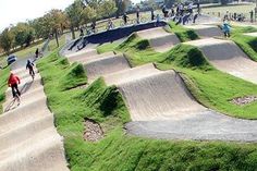 many people are riding their bikes on the skateboard ramps in a park with green grass