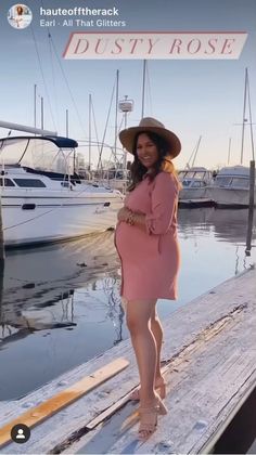 a woman in a pink dress and hat standing on a dock next to some boats