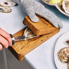 a person using a knife to cut clams on a cutting board with a wooden block