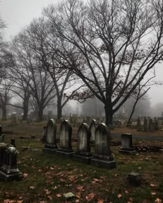 an old cemetery with tombstones and trees in the background on a foggy day