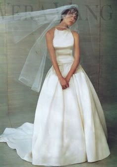 a woman in a white wedding dress with a veil over her head and hands behind her back