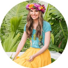 a woman with flowers in her hair sitting on a bench wearing a yellow skirt and blue shirt