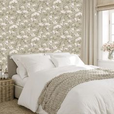 a white bed sitting under a window next to a wallpaper covered in flowers and leaves