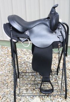 a close up of a black saddle on a stand with gravel in the foreground