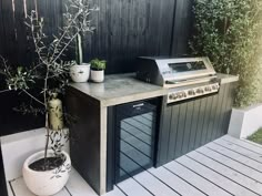 an outdoor kitchen with a grill and potted plants on the counter top next to it