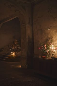 candles are lit in an old room with flowers and vases on the table next to it