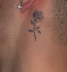 a man with a rose tattoo on his neck and behind his ear is a piercing