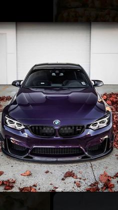 a purple car parked in front of a garage door with leaves on the ground around it