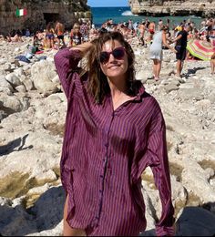 a woman is standing on the beach with her arms behind her head and people in the background