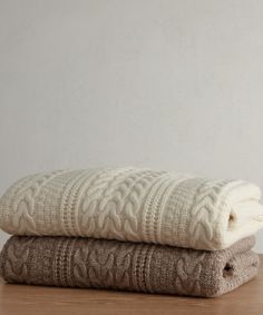 two blankets folded on top of each other sitting on a wooden table next to a white wall