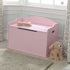 a pink toy box sitting on top of a rug next to a teddy bear and window