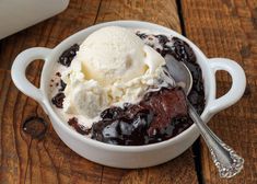 a bowl filled with ice cream and chocolate sauce on top of a wooden table next to a spoon