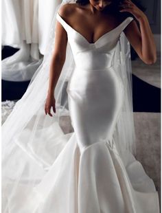 a woman in a white wedding dress is looking down at her hair and wearing a veil