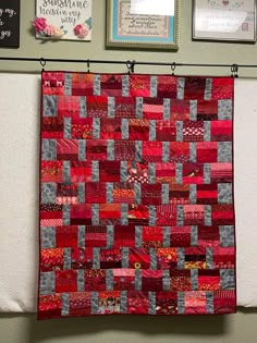 a red and grey quilt hanging on a wall next to framed pictures with writing on it