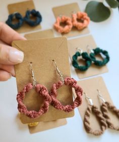 a person holding up some earrings on top of a piece of paper with other items in the background