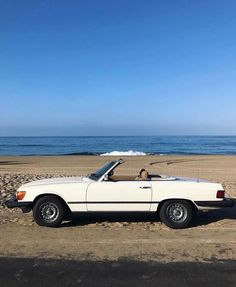 a white convertible car parked on top of a sandy beach next to the ocean and blue sky