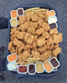 a tray filled with chicken nuggies and dipping sauces next to someone's feet