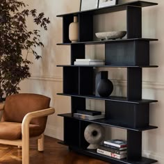 a black book shelf sitting on top of a hard wood floor next to a chair