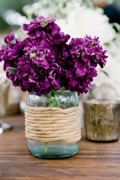 some purple flowers are in a glass vase on a table with twine wrapped around it