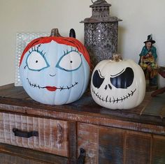 three painted pumpkins sitting on top of a wooden dresser next to a candle holder