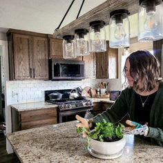 a woman preparing food in a kitchen with mason jars hanging from the ceiling above her