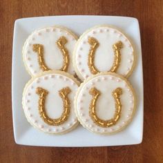 four decorated cookies on a white plate with gold icing and the letter u spelled out