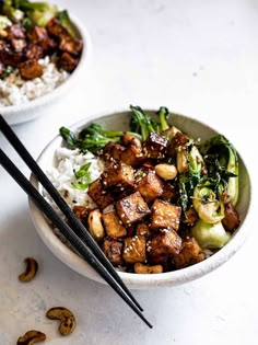 two bowls filled with food and chopsticks on top of a white countertop