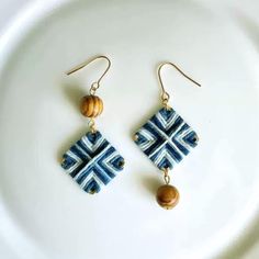 a pair of blue and white earrings sitting on top of a white plate next to a wooden bead