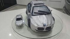 a silver car cake sitting on top of a glass plate next to a toy car