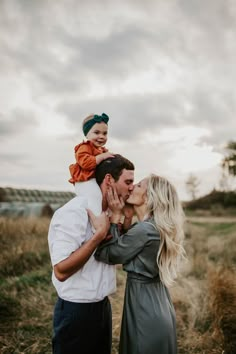 a man and woman kissing while holding a baby in their lap, with the child on his shoulders