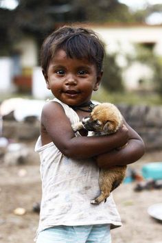 a little boy holding a small animal in his arms and smiling at the camera with one eye open