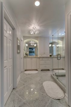 an elegant bathroom with marble floors and white cabinets, chandelier, shower stall and glass door