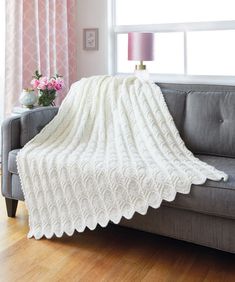 a white blanket sitting on top of a gray couch next to a pink flower vase